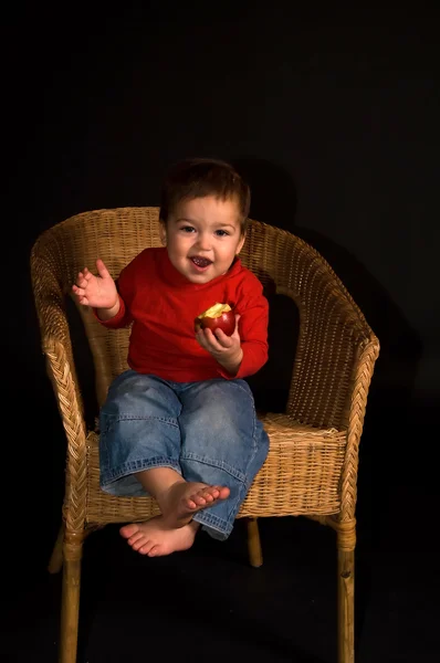 Junge sitzt im Sessel und isst Apfel — Stockfoto