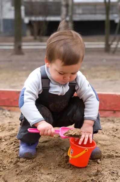 Child sitting in sandbox making mud pie — Stock Photo, Image