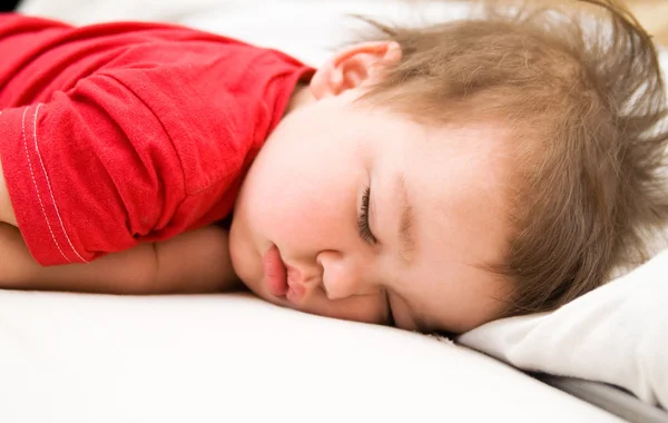 Pojke i röd klänning sova på sängen — Stockfoto