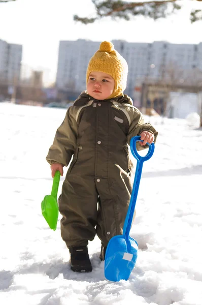 Thoughtful baby with shovels against bui — Stock Photo, Image