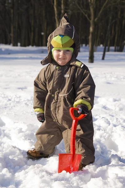 Bambino con pala rossa contro la neve — Foto Stock
