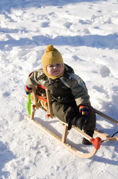 Baby in green coat sitting in sled — Stock Photo, Image