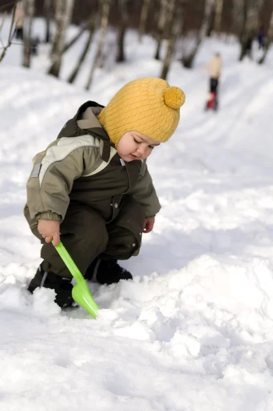 Baby met groene schop tegen sneeuw — Stockfoto