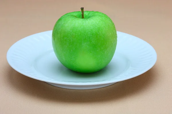 Green apple on white plate — Stock Photo, Image