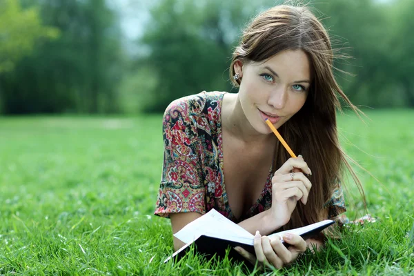 Žena se položí na trávě v parku s deník v rukou — Stock fotografie