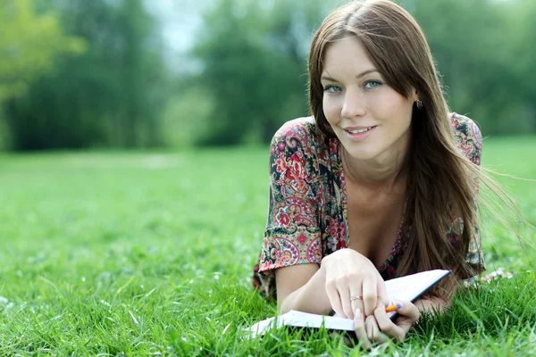 Mulher põe em uma grama no parque com um diário em mãos — Fotografia de Stock