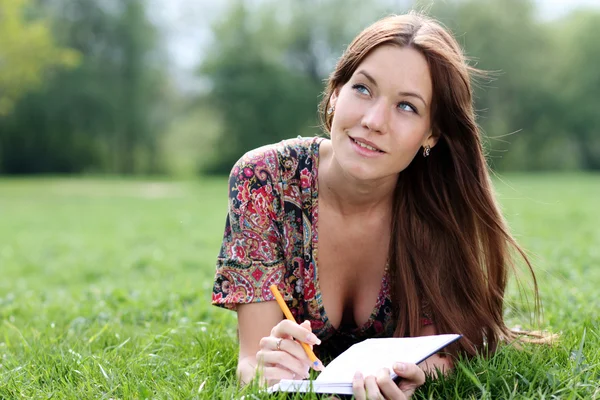 Frau legt sich mit Tagebuch in der Hand auf Gras im Park — Stockfoto