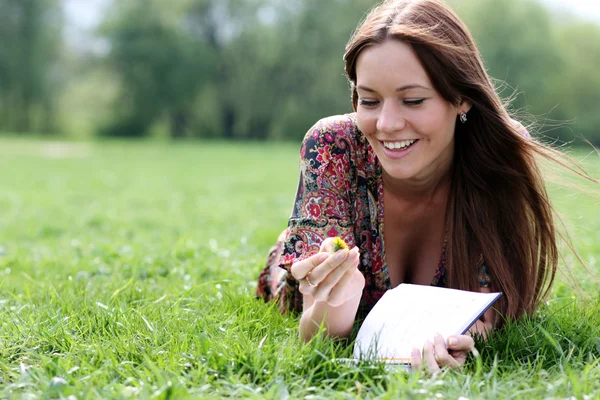 La mujer yace sobre una hierba en el parque con un diario en las manos — Foto de Stock