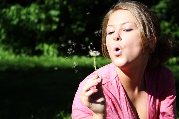 Young woman blowing on the dandelion — Stock Photo, Image