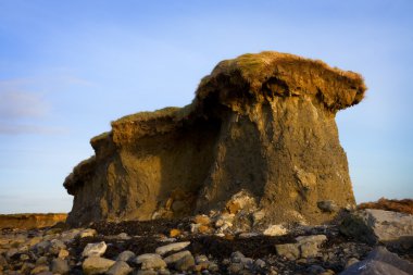 Lone cliff on stony beach clipart