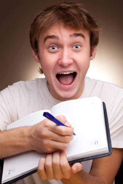 Ένα αστείο νεαρός άνδρας που γράφει σε ένα σημειωματάριο — Φωτογραφία Αρχείου