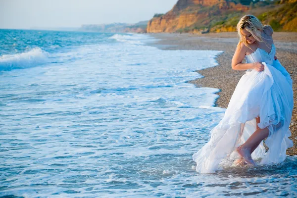 Bride running away from sea waves — Stock Photo, Image