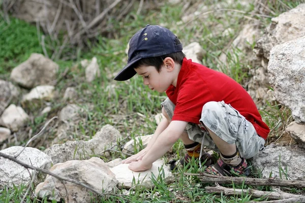Little boy squatting on stones outdoors — Stock Photo, Image