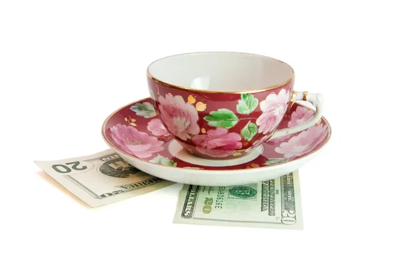 Tea cup and saucer on dollar bills — Stock Photo, Image