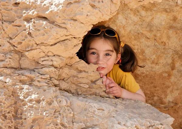 Linda niña se esconde detrás de una roca — Foto de Stock