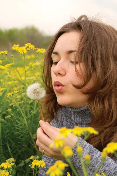 Beautiful woman blowing dandelion seeds — Stock Photo, Image