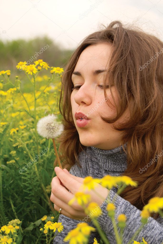 Beautiful woman blowing dandelion seeds