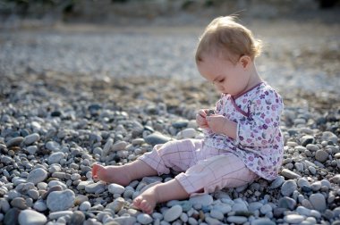 Little baby sitting on the stones by the clipart