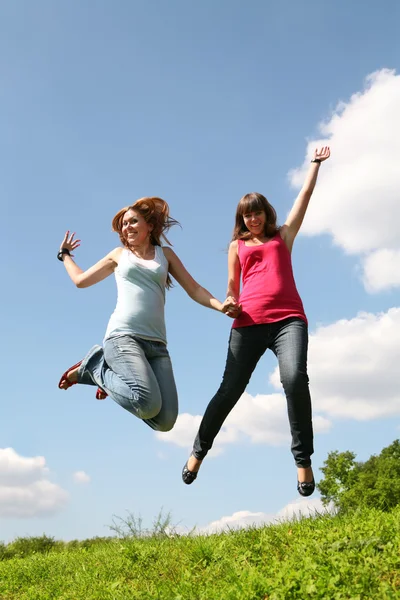 Two girls jump under blue sky