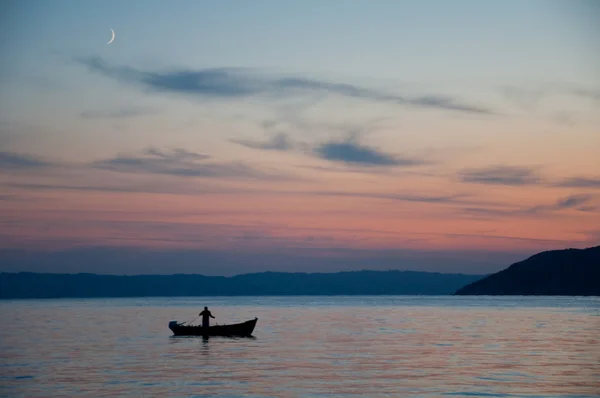 Západ slunce, rybář se sítěmi na své lodi — Stock fotografie