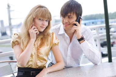 Couple sitting in cafe using their cell clipart