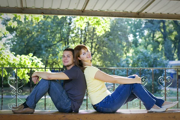Couple sitting back to back on a bench — Stock Photo, Image