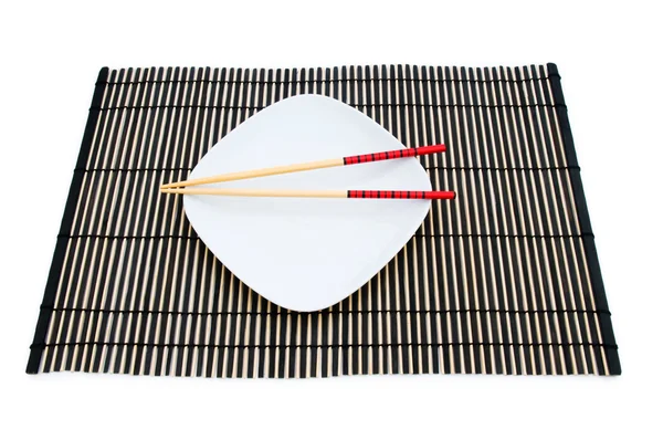 Yemek çubukları ve bambu hasır üzerinde plaka — Stok fotoğraf