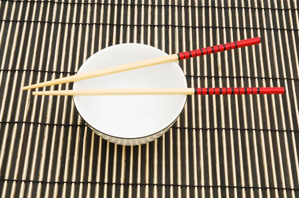 Eetstokjes en kom op de bamboe mat — Stockfoto