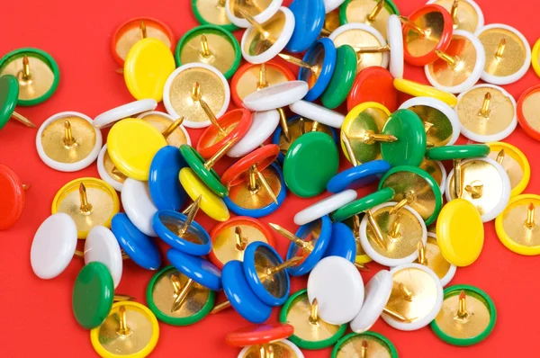 Many colourful office pins on red — Stock Photo, Image