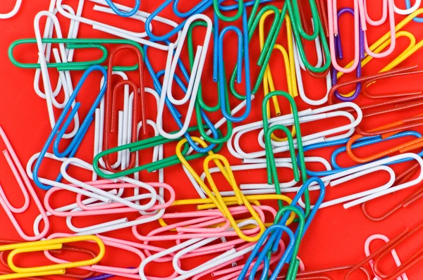 Vele kleurrijke paperclips op rood — Stockfoto