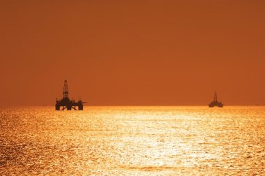 Two offshore oil rigs during sunset clipart