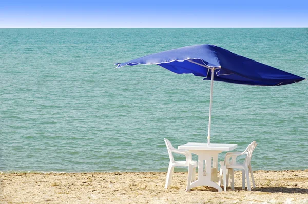 Pöytä, tuolit ja päivänvarjo rannalla — kuvapankkivalokuva
