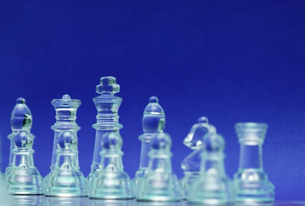 Стеклянные шахматные фигуры над синим — стоковое фото