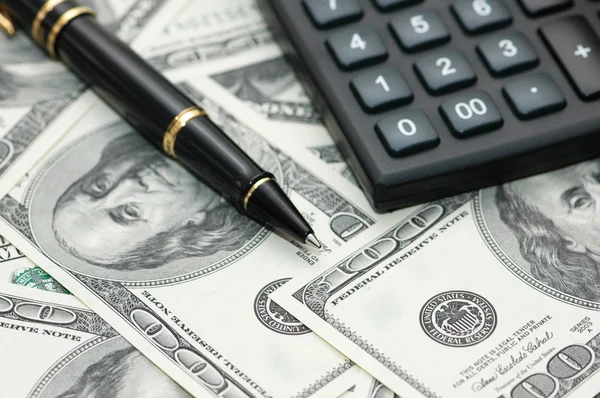 Калькулятор и ручка над долларами — стоковое фото