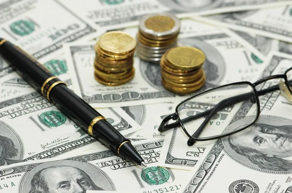 Moedas, caneta e óculos sobre os dólares — Fotografia de Stock