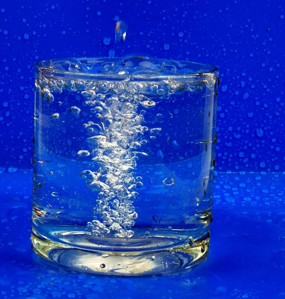 Glas water en druppels op een donkere backg — Stockfoto