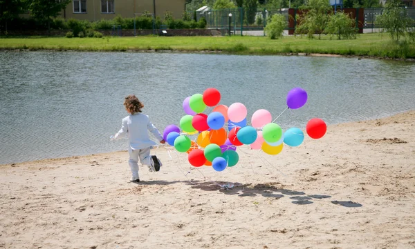 Little boy runs with helium bubbles on s — Stock Photo, Image