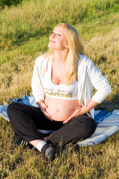 Mulher grávida sentada na grama e — Fotografia de Stock