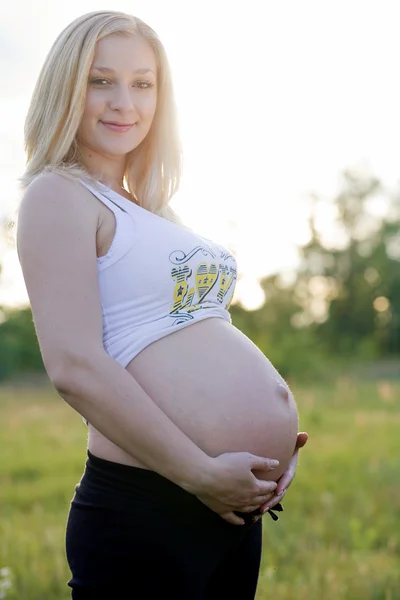 Těhotná žena hospodářství břicho na louce — Stock fotografie