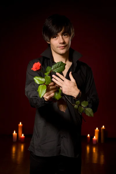 stock image Young man with rose in black shirt on red backg