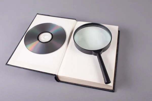 Opened book with magnifying glass and cd — Stock Photo, Image