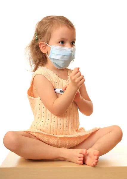 Flicka är i en medicinsk mask med en termometer — Stockfoto