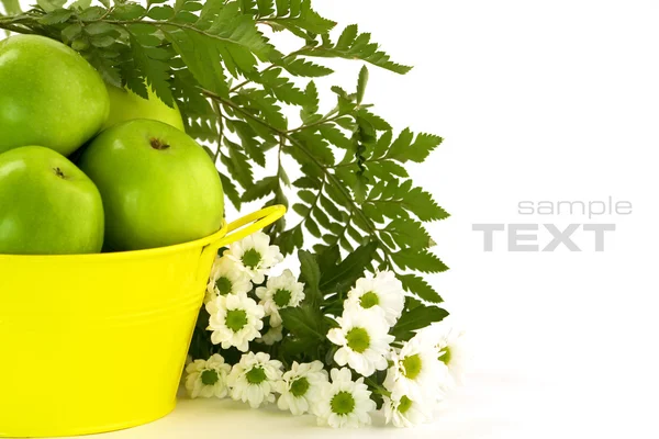 Green apples, yellow bucket and flowers — Stock Photo, Image