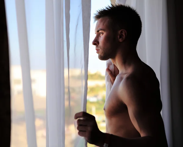 Mladá atraktivní macho v okně — Stock fotografie