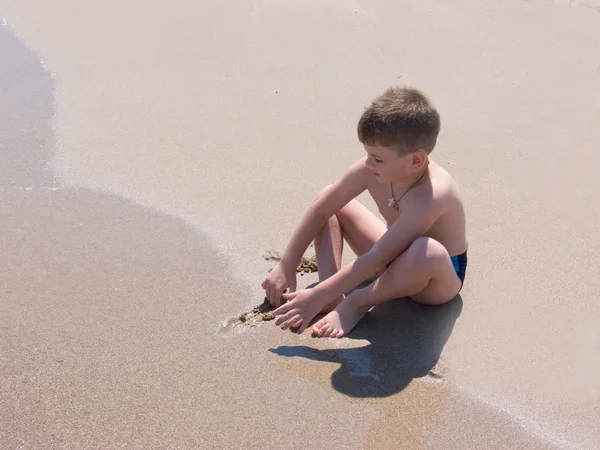 Niño se sienta en la costa — Foto de Stock