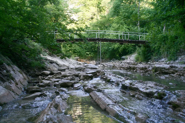 Маленькая горная река течет под мостом — стоковое фото