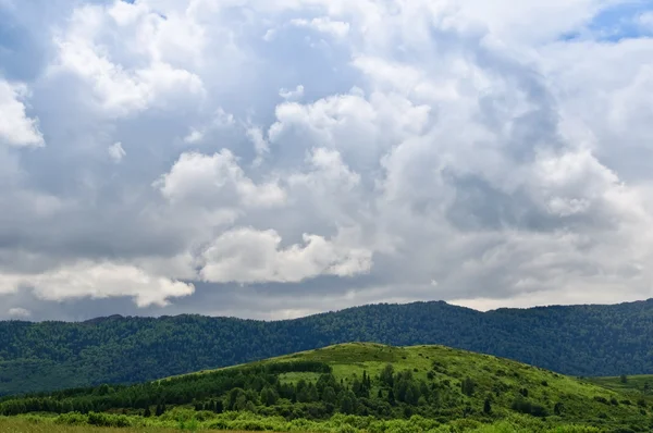 Pastagem contra montanhas e nuvens — Fotografia de Stock