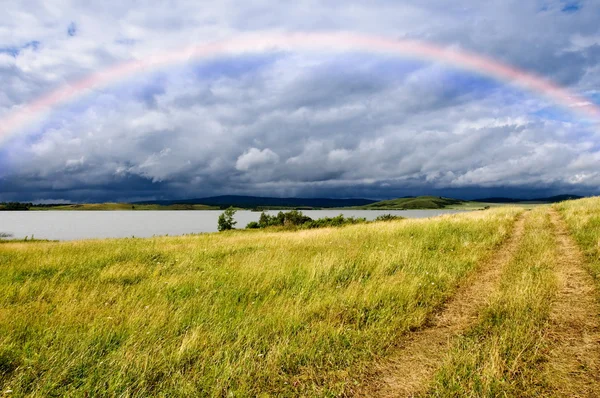 Field road and rainbow over lake — Stock Photo, Image