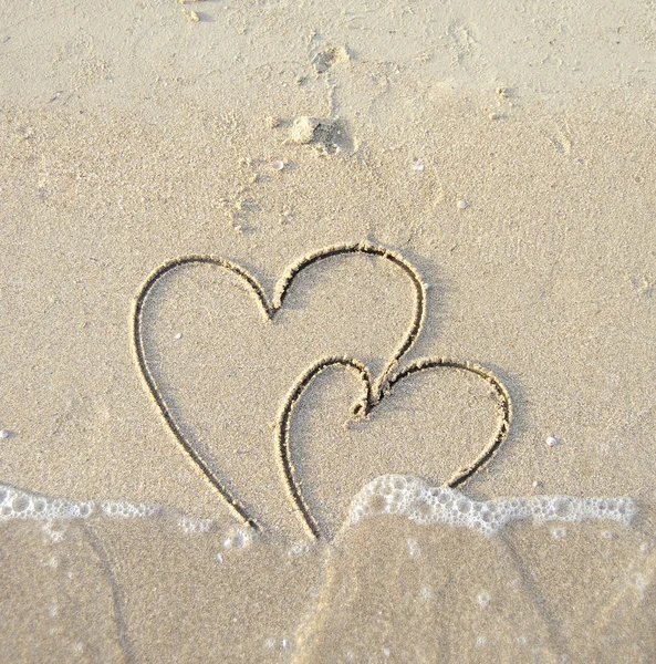 Dos corazones conectados dibujados sobre arena mojada — Foto de Stock
