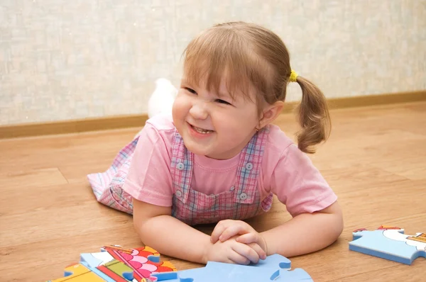 Klein meisje verzamelt puzzels in een kamer — Stockfoto